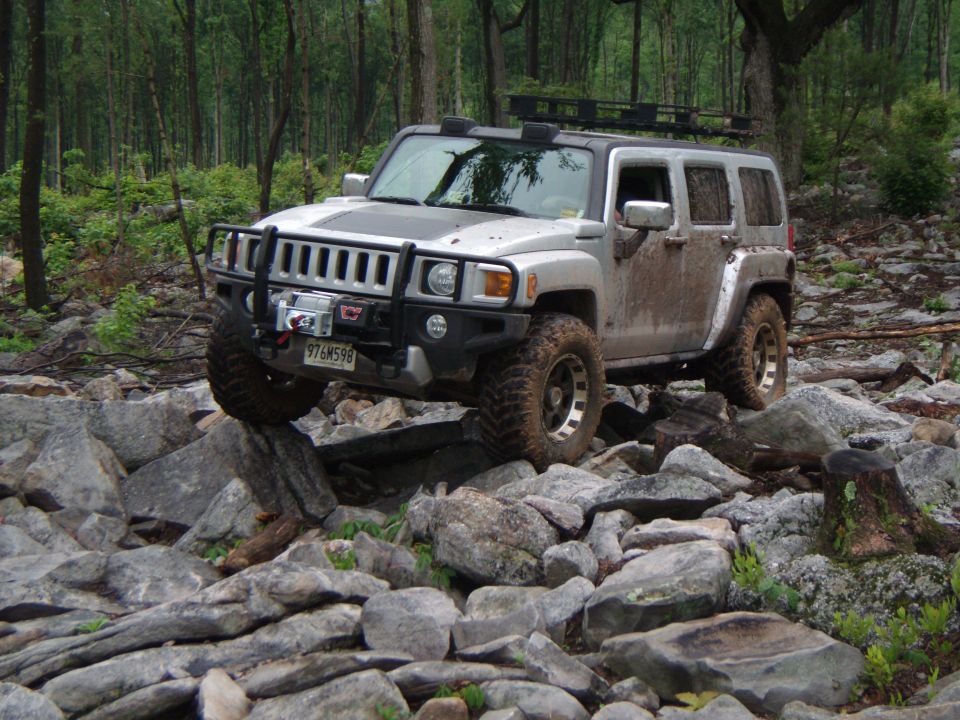 Silver Hummer H3 driving over rocks on a wooded trail. Winch on front bumper