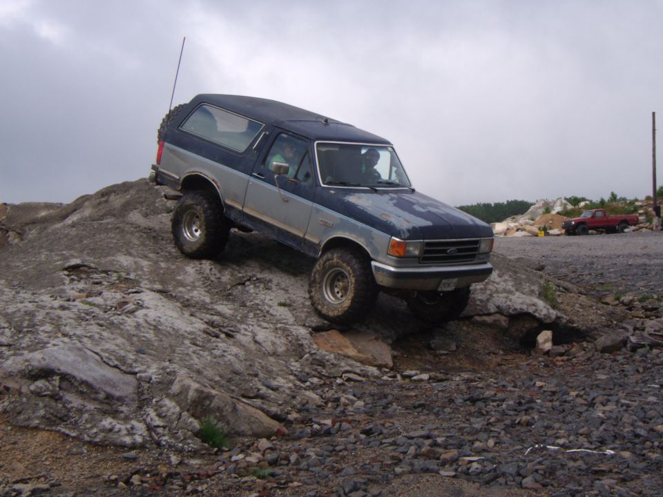 1987 Ford Bronco climbing rocky terrain, another red truck in background