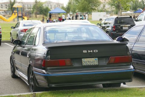 1990 Ford Taurus - A black 1990 Ford Taurus SHO is parked next to another car, with a playground in the background.