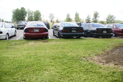 1990 Ford Taurus - Several cars are parked in a lot, including a black Ford Taurus SHO with tinted taillights.
