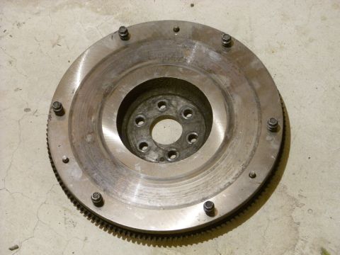 1988 Ford Bronco - A circular metal part with a toothed edge and several bolt holes is shown resting on a concrete surface.