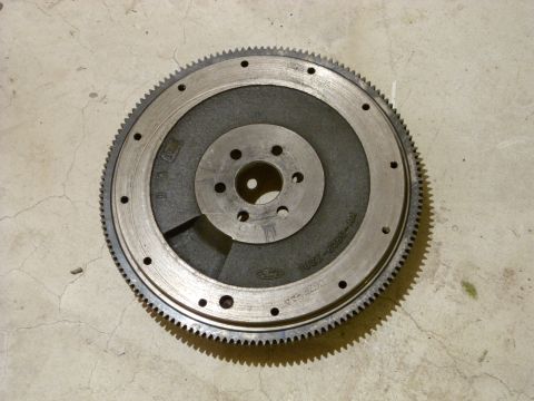 1988 Ford Bronco - A Ford flywheel sits on a concrete surface, showing its gear teeth and center mounting holes.