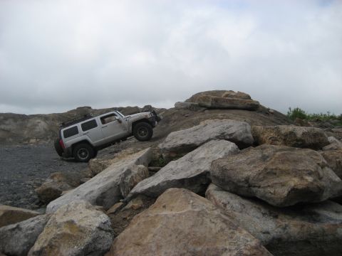 1991 Ford Bronco - A silver Hummer H3 navigates a challenging rocky obstacle course under an overcast sky.