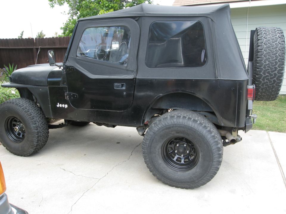 Black Jeep CJ7 with soft top and spare tire on rear. "Jeep" badge visible on fender