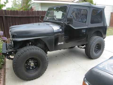 1986 Ford Bronco - This black Jeep CJ7 is shown from a three-quarter front angle, equipped with off-road tires and a soft top.