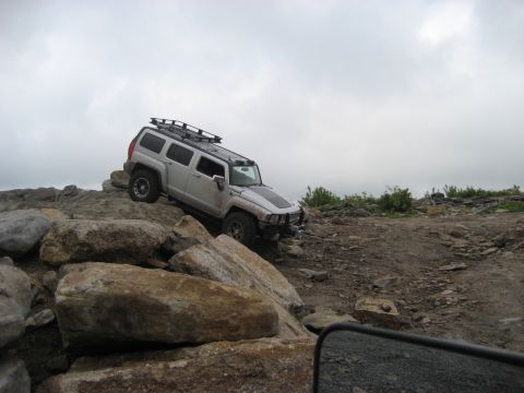 1991 Ford Bronco - Hummer H3 navigating a rocky off-road course under an overcast sky.