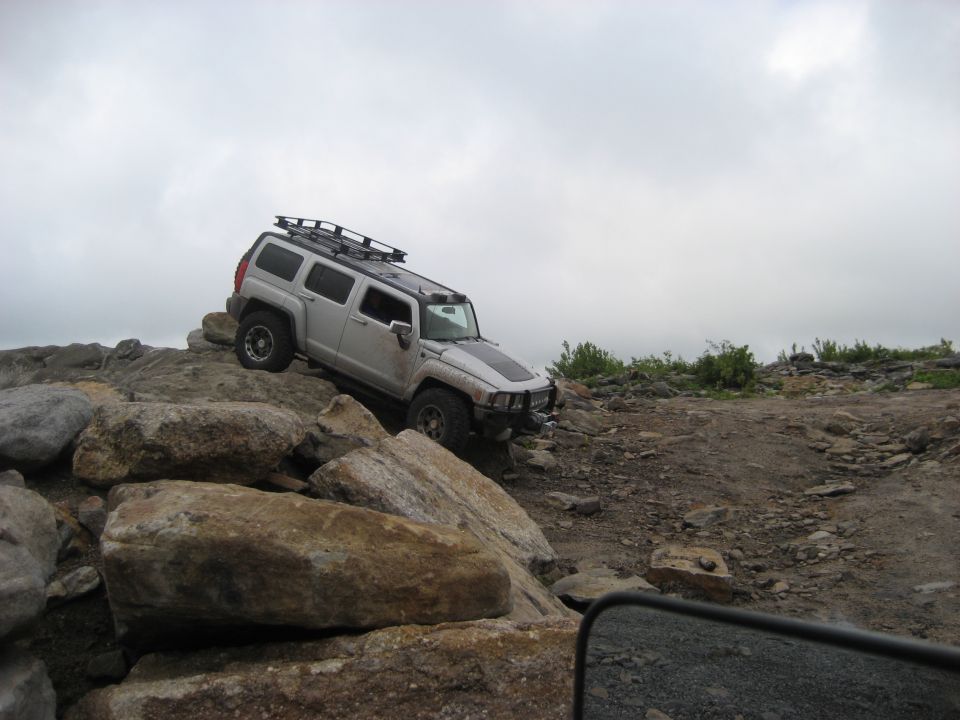 Silver Hummer H3 climbing over large rocks on a trail. Roof rack installed