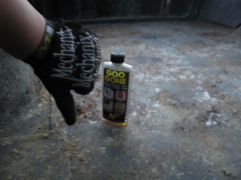 1986 Ford Bronco - A bottle of Goo Gone sits on the floor of a vehicle, with a gloved hand nearby.