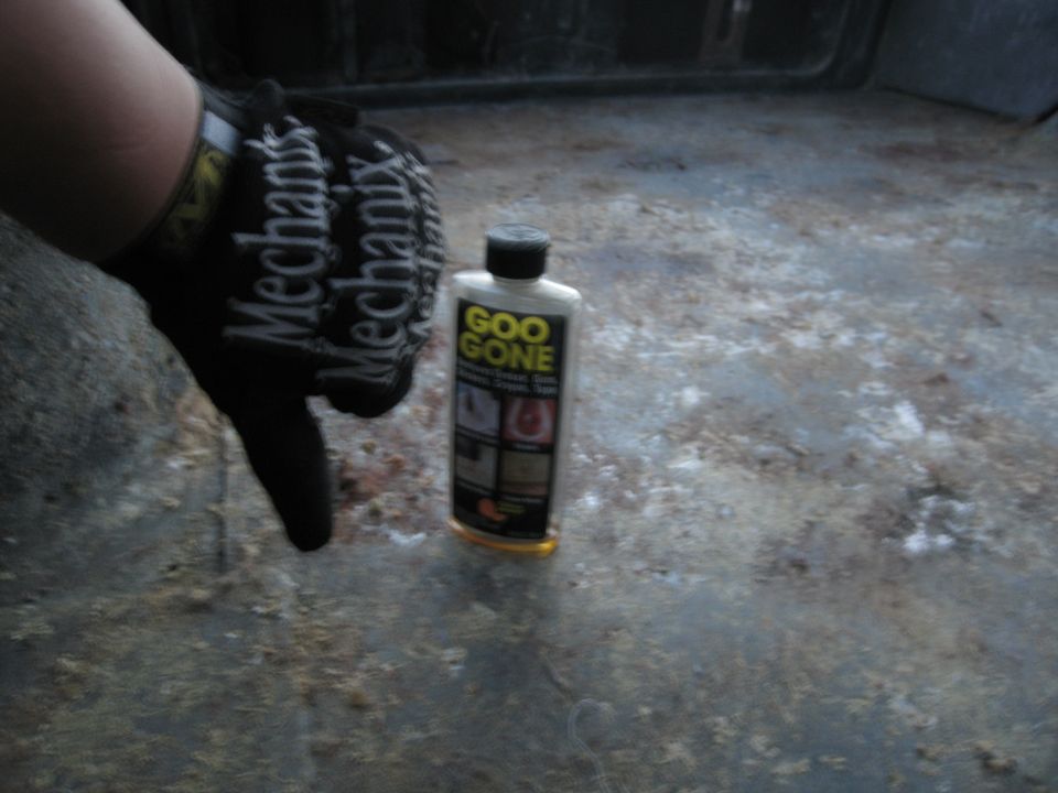 Goo Gone bottle on dirty vehicle floor, hand in Mechanix glove pointing