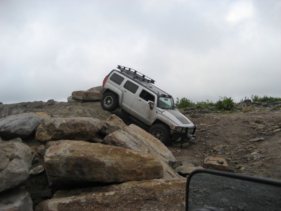 Silver Hummer H3 climbing over large rocks on an off-road trail