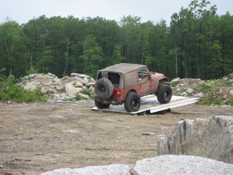 1991 Ford Bronco - A red Jeep Wrangler is positioned on a white platform in an outdoor, rocky area.