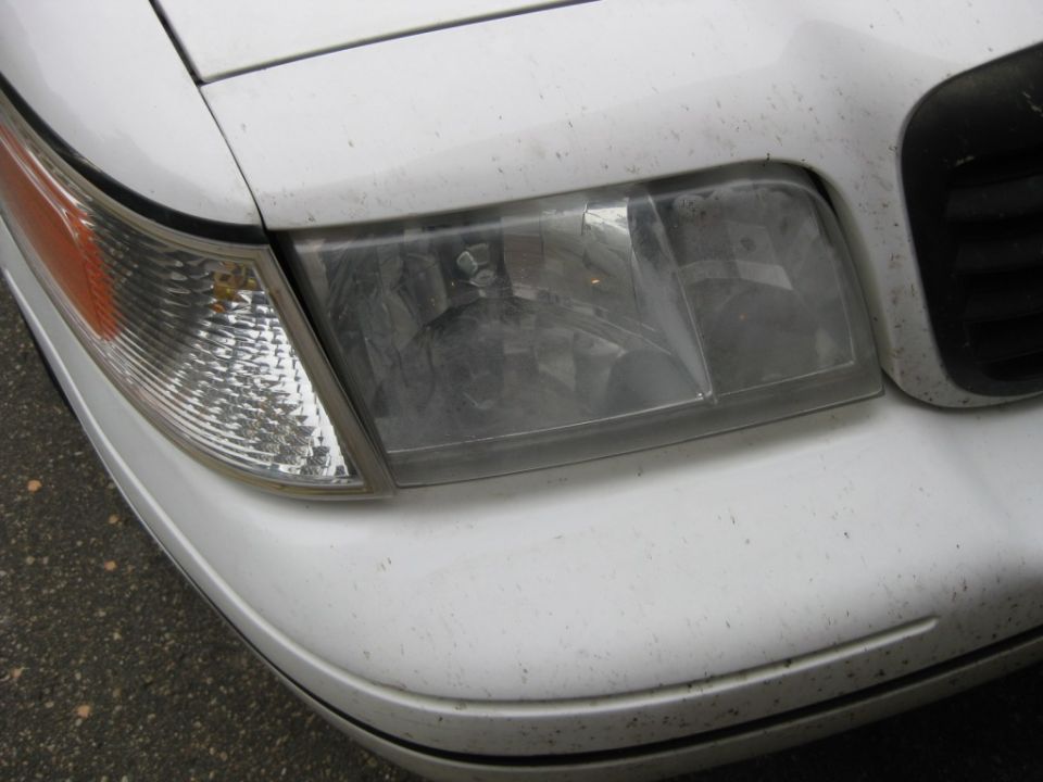 Close-up of the front corner of a white car, showing the headlight and turn signal