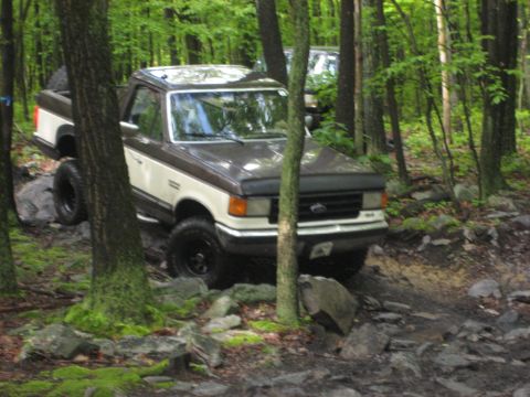 1991 Ford Bronco - 1991 Ford Bronco navigating a rocky trail through a dense forest with another vehicle following.