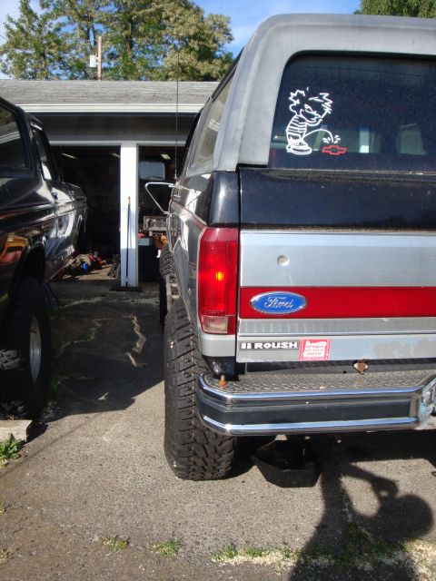 1989 Ford Bronco - A modified Ford Bronco is parked next to another vehicle, with a 'Roush' sticker visible on its tailgate.