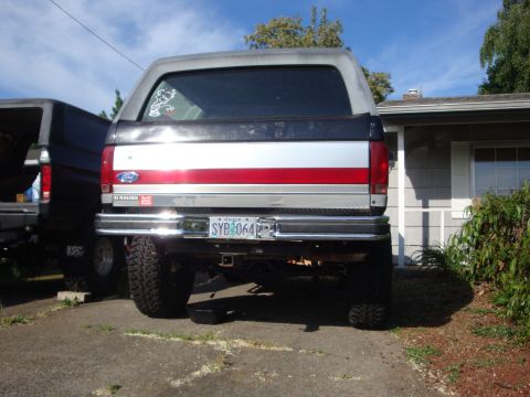 1989 Ford Bronco - Lifted 1987 Ford Bronco seen from the rear, parked next to another vehicle in a driveway.