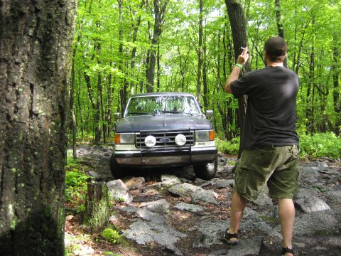 1991 Ford Bronco - A Ford Bronco navigates a challenging rocky path through a dense forest.