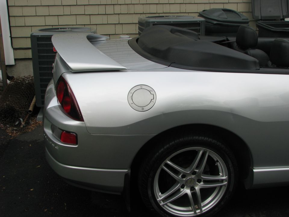 Silver convertible sports car rear quarter panel, gas cap, spoiler, and taillight. Black soft top is up