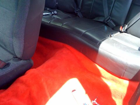 2003 Ford Crown Victoria - Interior view of a vehicle showing bright red carpet and black leather rear seats with seatbelts.