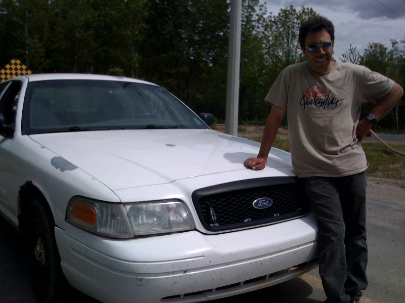 White Ford Crown Victoria sedan, front 3/4 view, man leaning on hood outdoors