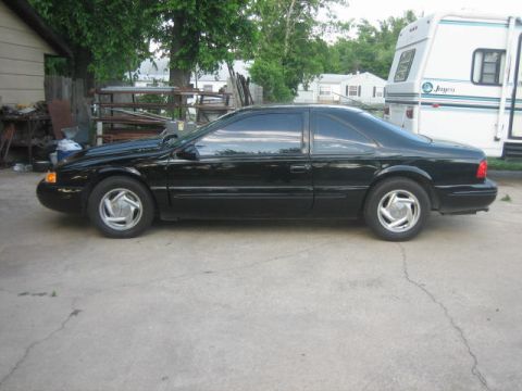 1996 Ford Thunderbird - Side profile of a black 1996 Ford Thunderbird coupe parked on a concrete driveway.