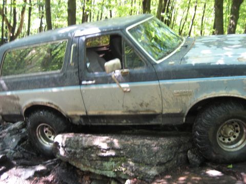 1991 Ford Bronco - This Ford Bronco is navigating a rocky trail in a wooded area.