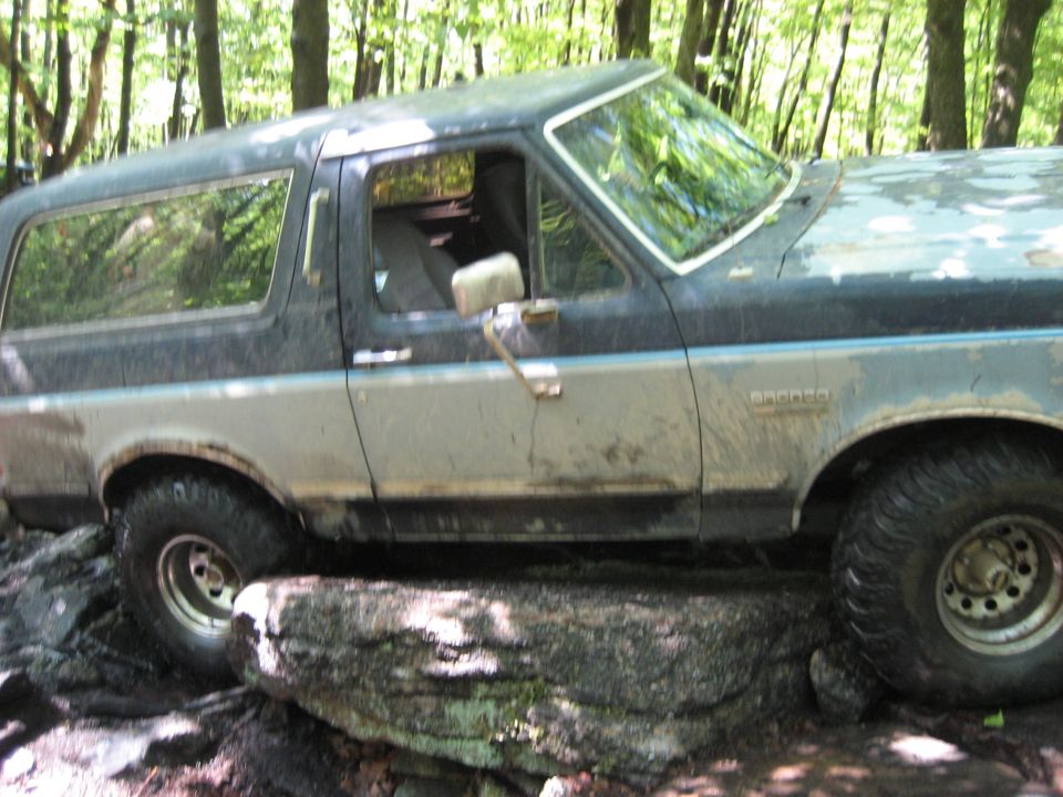 Mud-splattered two-tone Ford Bronco on a rock obstacle