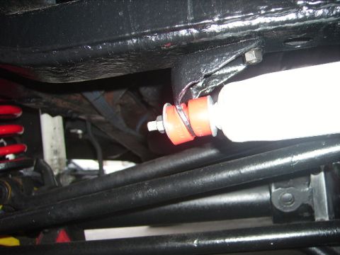 1978 Ford Bronco - Close-up of a suspension component, likely a shock absorber mount with red bushings, viewed from underneath a vehicle.