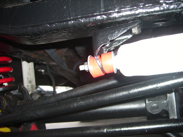 Underbody view of a red suspension bushing and white shock absorber