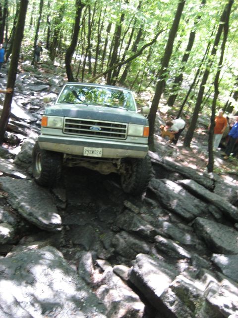 1991 Ford Bronco - A Ford Bronco is driven over large rocks on a wooded trail.