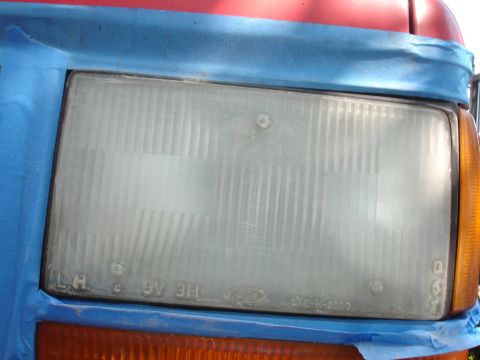 1992 Ford Explorer - Close-up of a vehicle's headlight assembly, partially covered by blue masking tape.