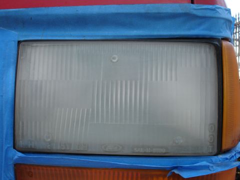 1992 Ford Explorer - Close-up of a vehicle's headlight assembly, partially covered with blue painter's tape.