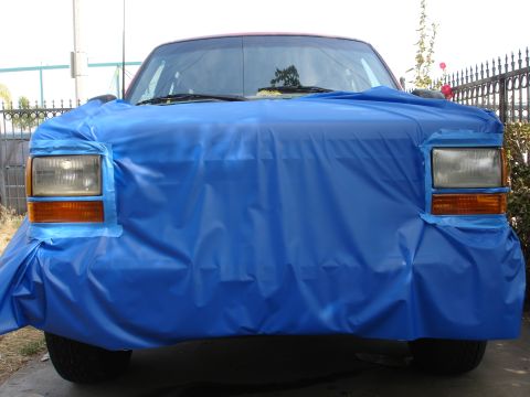 1992 Ford Explorer - The front of a vehicle is covered in a blue tarp, with only the headlights and orange turn signals exposed.