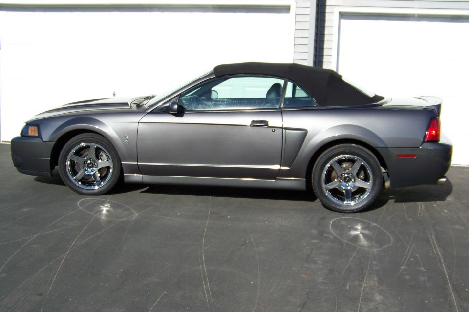 Gray Ford Mustang convertible parked on asphalt in front of a garage