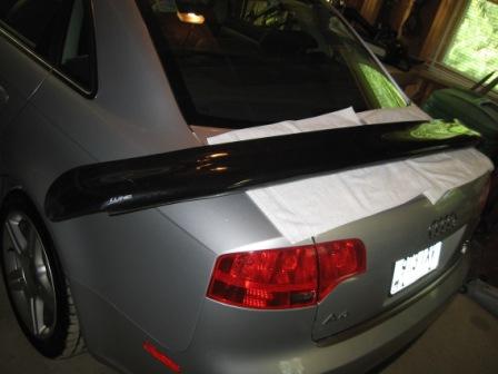 1993 Ford Bronco - A black rear spoiler is placed on the trunk of a silver Audi sedan, ready for installation.