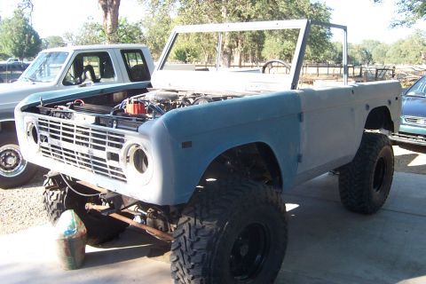 1976 Ford Bronco - Ford Bronco undergoing restoration, showing its front end with an open hood and primer-gray fenders.