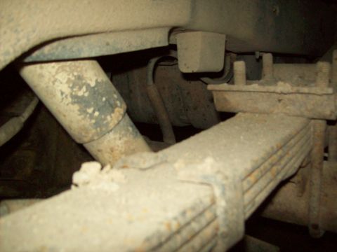 1985 Ford Bronco - The underside of a vehicle shows heavily rusted leaf springs and a shock absorber, indicating significant wear.