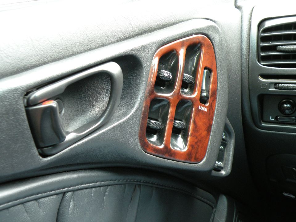 Interior door panel with chrome handle, wood trim around power window switches, and a lock button