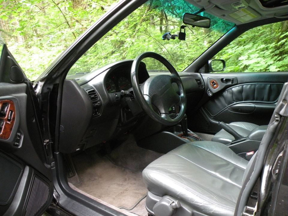 Black car interior with gray leather seats, dashboard, and steering wheel. Trees visible through windows