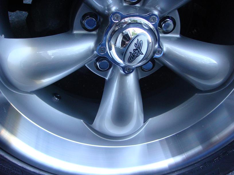 Close-up of a silver five-spoke wheel with a chrome center cap a circular logo with stylized text inside