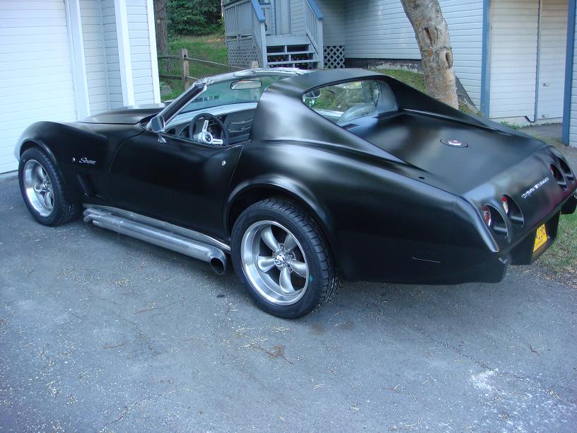 Black 1975 Chevrolet Corvette with side pipes and aftermarket wheels parked on asphalt