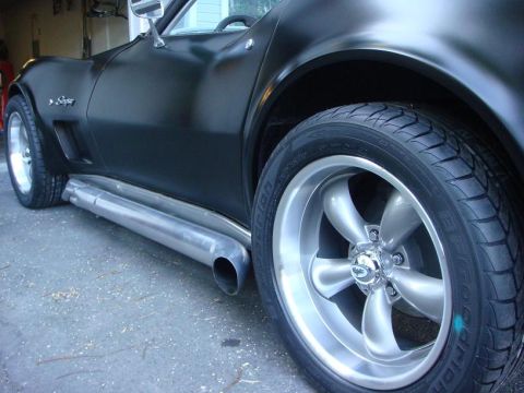 1975 Chevrolet Corvette - A black 1975 Chevrolet Corvette is shown from the side, custom wheels and prominent side exhaust pipes.