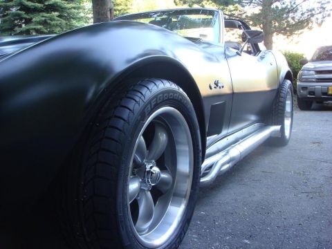 1975 Chevrolet Corvette - Close-up of a 1975 Corvette's front fender, wheel, and side pipes, with another vehicle in the background.