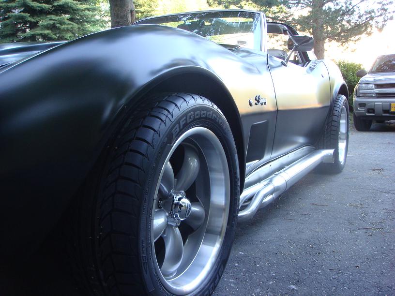 1975 Chevrolet Corvette convertible with aftermarket wheels and side pipes, parked next to an SUV