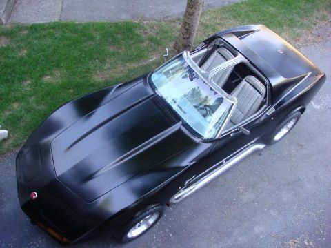 1975 Chevrolet Corvette - A black 1975 Chevrolet Corvette with chrome side pipes and T-tops is parked on asphalt.