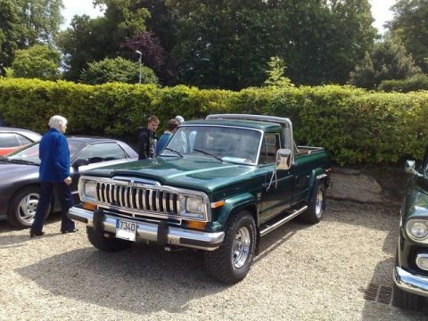1991 Ford Crown Victoria - A green pickup truck is parked on a gravel lot with other vehicles and people nearby.