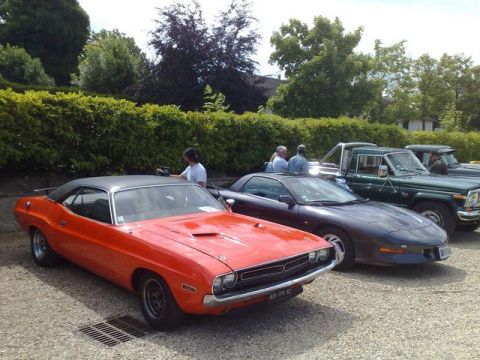 1991 Ford Crown Victoria - An orange 1970s muscle car, possibly a Dodge Challenger, is parked at a car show with other vehicles in the background.