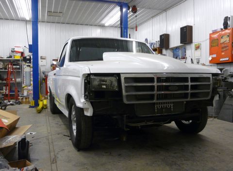 1994 Ford F-150 - Front view of a white pickup truck with a custom hood, undergoing modifications in a workshop.