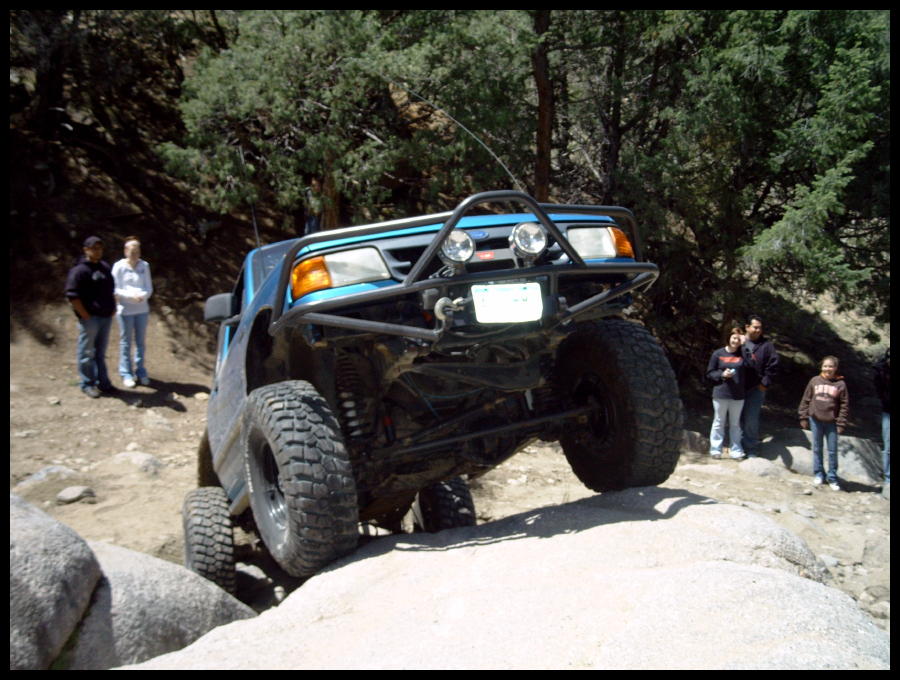 Blue off-road SUV with a custom bumper and large tires navigating rocky terrain