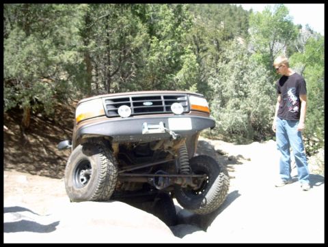 1993 Ford Bronco - A 1993 Ford Bronco is shown off-roading on a rocky trail with a person standing nearby.
