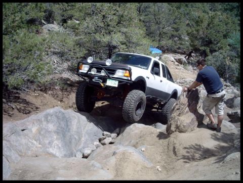1993 Ford Bronco - A modified pickup truck is carefully driven over large rocks on a steep, off-road trail.